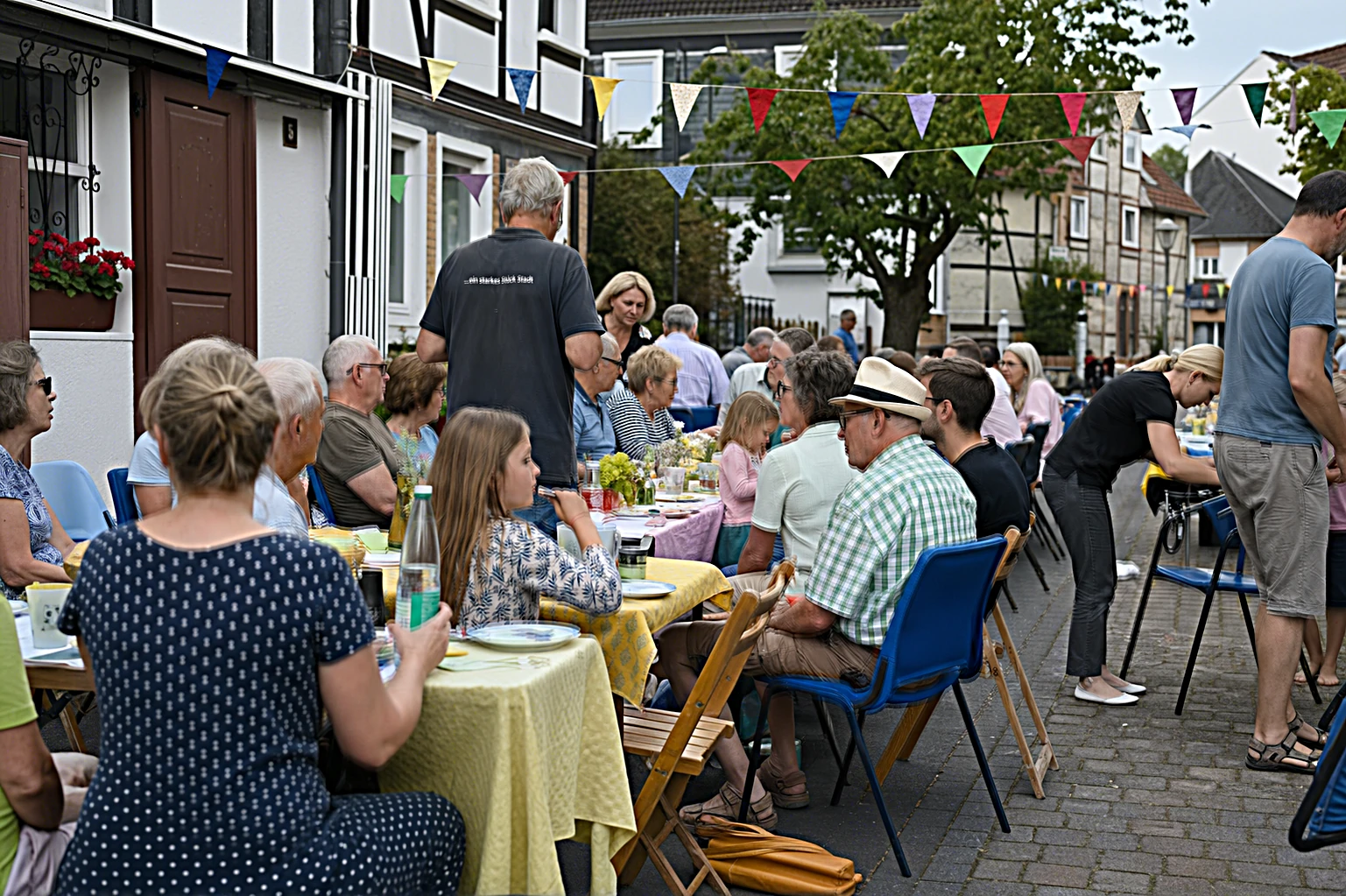 Nachbarn feiern ein sommerliches Straßenfest mit langen Tischen und Girlanden